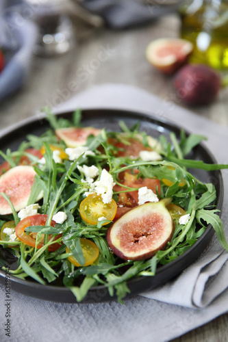 Fresh salad with arugula tomato and cheese on wooden background