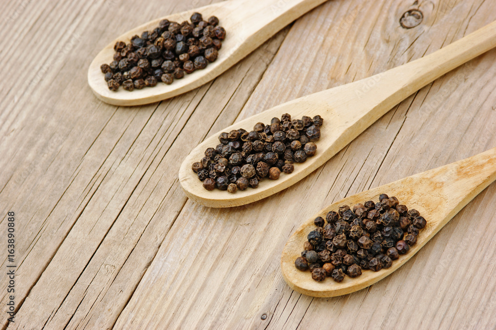 Black pepper in wooden spoon on the old board Black pepper in wooden spoon on the old board