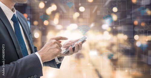 Business man using smart phone with wifi icon on blurred interior office space background - futuristic technology connection concept