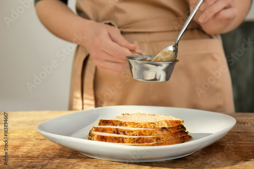 Tasty sliced turkey on plate and chef with gravy in small saucepan at table