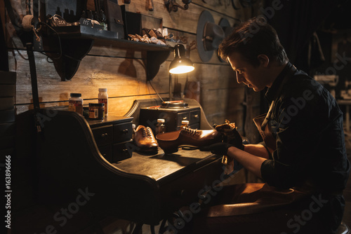 Concentrated man shoemaker at footwear workshop.
