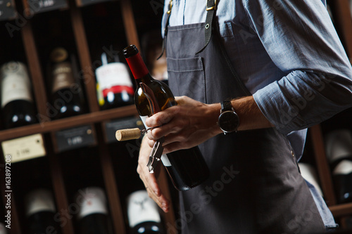Sommelier holding wine bottle in cellar on background of shelves