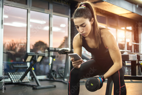 Young woman using phone at gym.