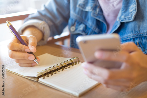 Wallpaper Mural Woman's hand writes spiral sheet and holds the phone on a wooden desk. Torontodigital.ca