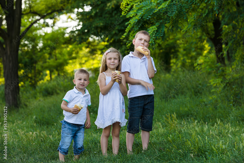 Sister and two brothers in the summer garden with picnic basket Sister and two brothers in the summer garden with picnic basket