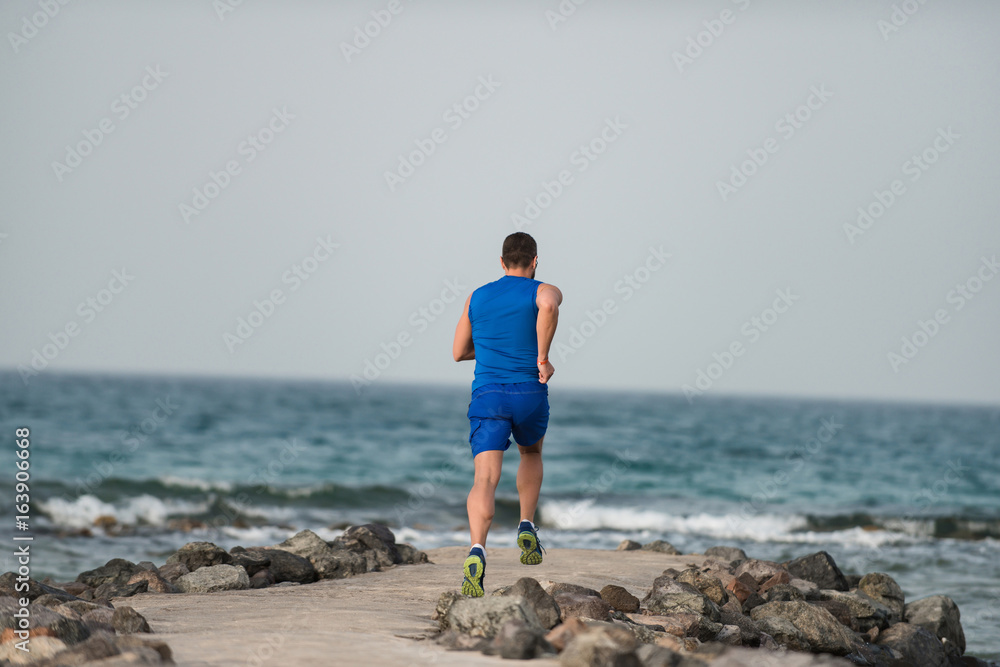 Runner boy in blue sportswear running along coast