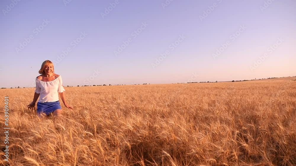 Amazing view of a cheerful blonde woman who runs along the splendid wheat field with ripe spikes and touches it with her hands on a sunny day in summer in slow motion. Amazing view of a cheerful blonde woman who runs along the splendid wheat field with ripe spikes and touches it with her hands on a sunny day in summer in slow motion.