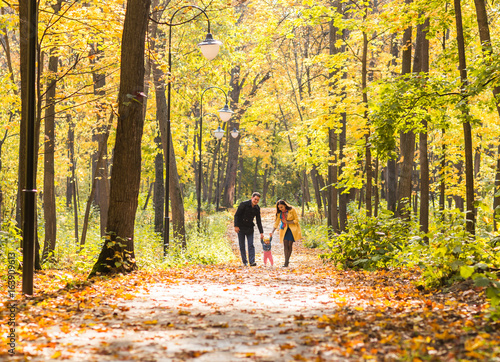 Happy young family in the autumn park outdoors on a sunny day. Mother  father and their little baby girl are walking in the park. Love and family concept.