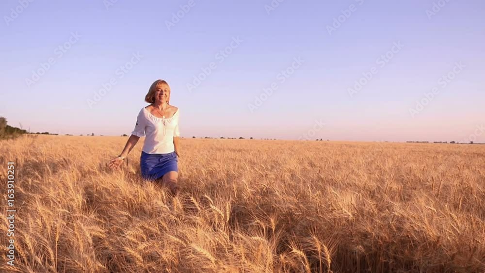 Amazing view of a happy young woman, dressed in embroidered Ukrainian shirt, who runs to the camera with hands aside in a wheat field at sunset in summer in slow motion. The skyscape is great Amazing view of a happy young woman, dressed in embroidered Ukrainian shirt, who runs to the camera with hands aside in a wheat field at sunset in summer in slow motion. The skyscape is great