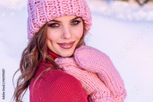 close up Winter portrait of a Happy candid beautiful young lady in a pink knitted beanie hat and gloves