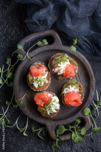 Delicious canape with salmon, cottage cheese, olive with micro greens on a dark background. Cold appetizer.