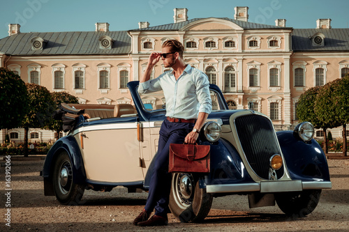 Tableau sur toile Confident wealthy young man with briefcase near classic convertible