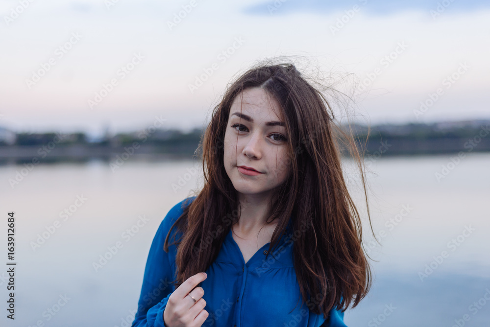 Summer happy portrait beautiful woman girl caucasian asian blended in blue shirt posing on background sky lake water sunset long hair brunette outdoors