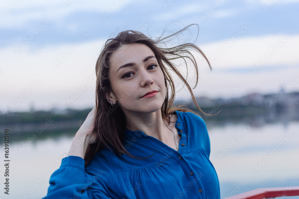 Summer happy portrait beautiful woman girl caucasian asian blended in blue shirt posing on background sky lake water sunset long hair brunette outdoors
