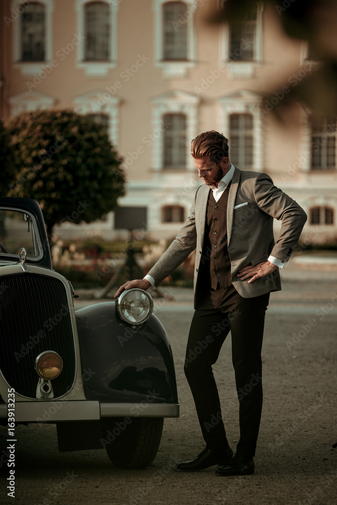 Naklejka premium Confident wealthy young man near classic convertible