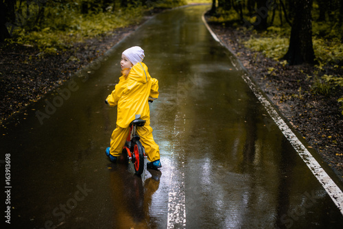 Little girl in yellow waterproof clothes on bike