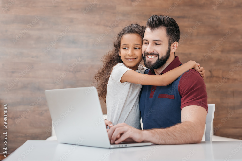 happy father using laptop while daughter hugging him