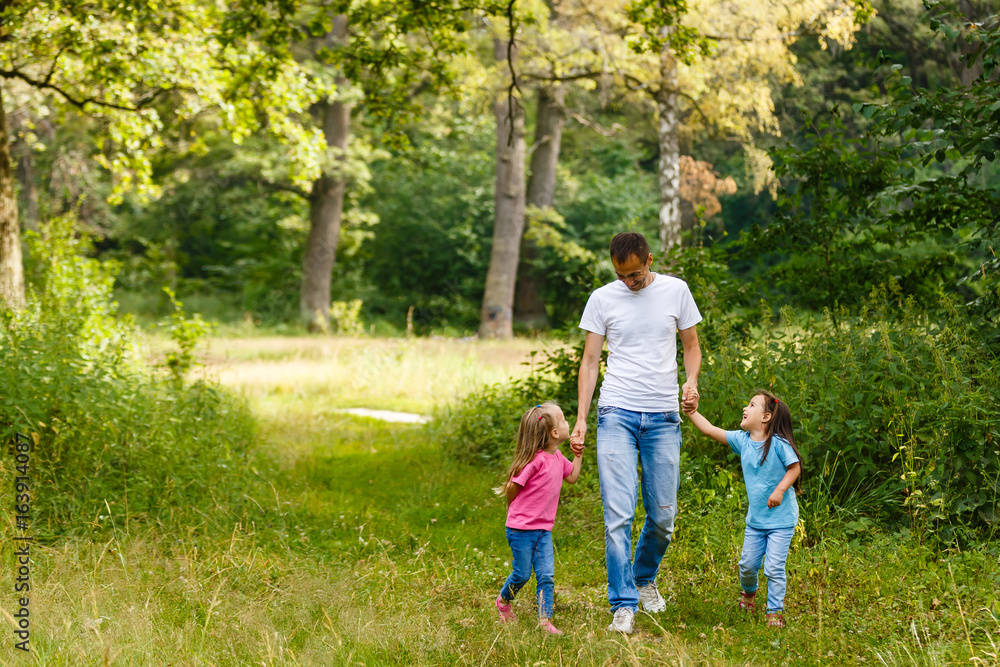 Fototapeta premium father enjoying spring walk with two smiling kid daughters. Family with two sisters happy together