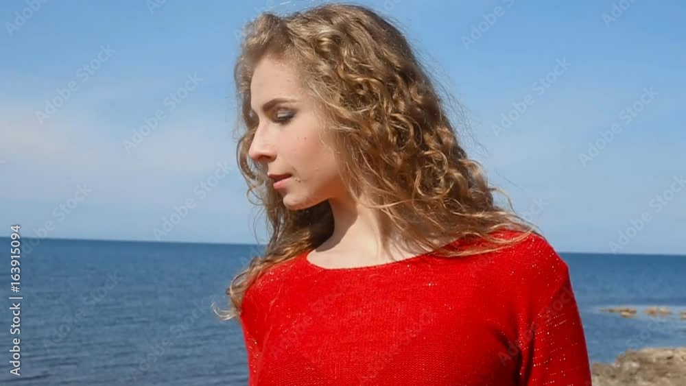 Close up portrait of woman running hand through curly hair blowing in wind by sea on beach. Happy female over blue sky Close up portrait of woman running hand through curly hair blowing in wind by sea on beach. Happy female over blue sky