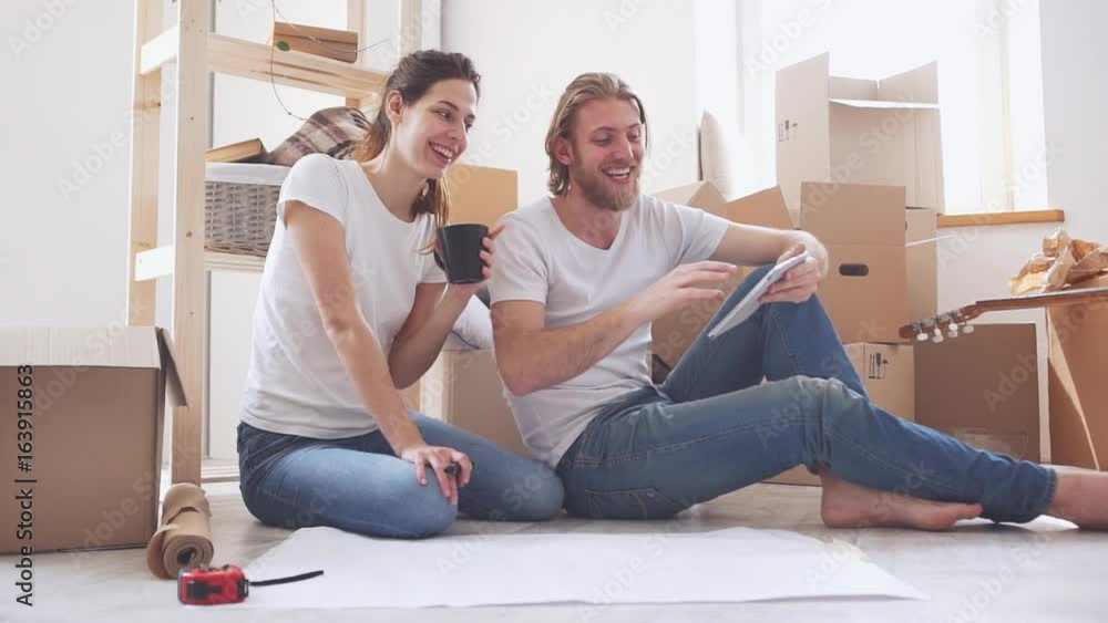 Happy Caucasian pair sitting on floor in new flat and discussing their future in slowmotion. Concept of home and peace Happy Caucasian pair sitting on floor in new flat and discussing their future in slowmotion. Concept of home and peace