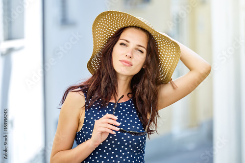 Beautiful young woman in a dress and a straw hat walks through the streets of a small town