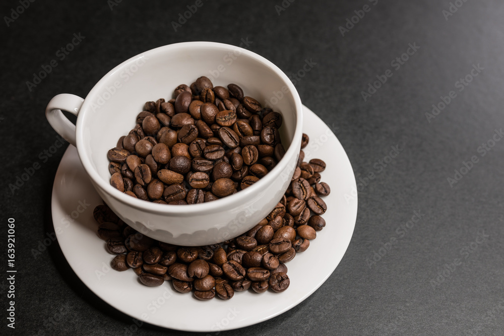 Roasted coffee beans in white cup on dark background. Selective focus. Roasted coffee beans in white cup on dark background. Selective focus.