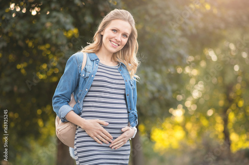 Cute young pregnant woman touching her belly in the park