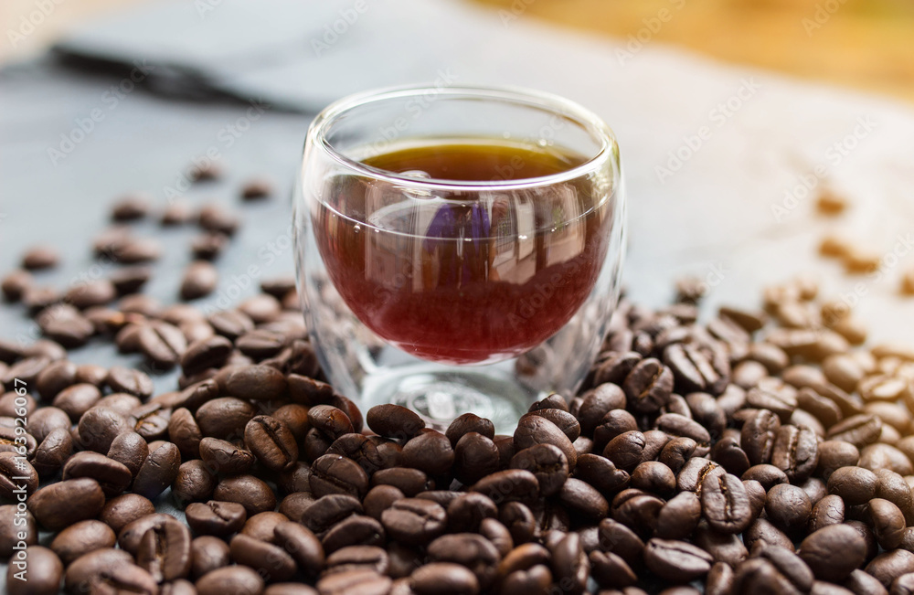 Black coffee in glass with bean coffee on black stone