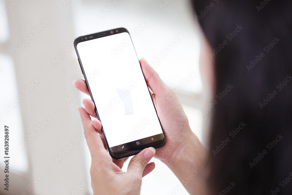 Women hands holding phone with isolated screen on background of window Women hands holding phone with isolated screen on background of window