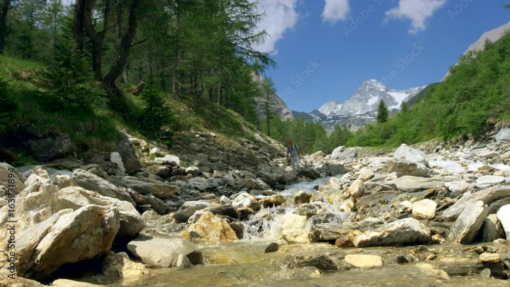 Hiker Walking on the Mountain River Boulders. Scenic Alpine River near Grossglockner, Austria. Hiker Walking on the Mountain River Boulders. Scenic Alpine River near Grossglockner, Austria.