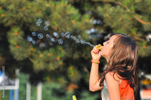 Adorable girl blowing soap bubbles in summer park. Girl play in park and blowing soap bubbles