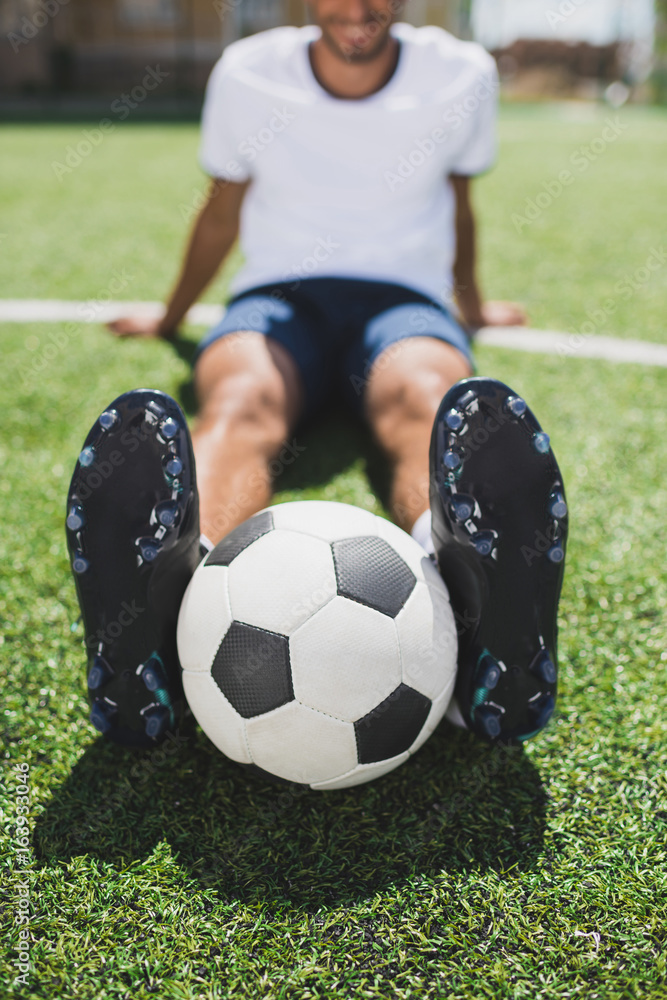 selective focus of soccer player with ball sitting on pitch