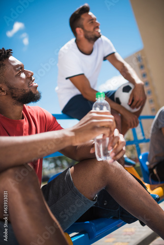 side view of african american man with water bottle resting on stadium