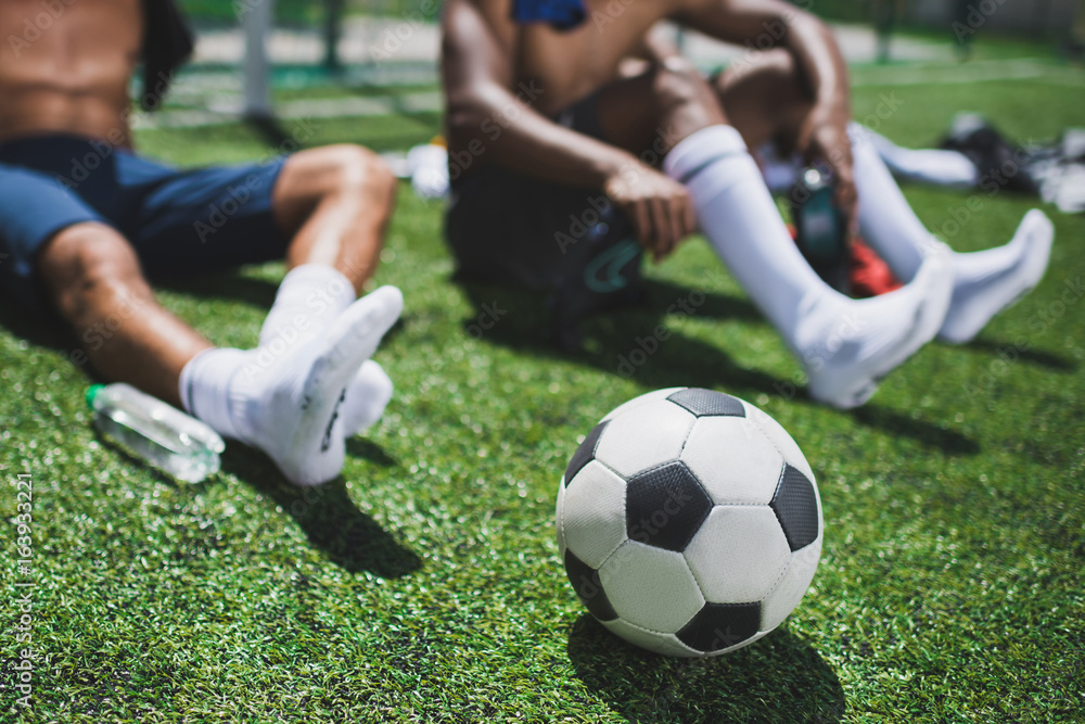 Fototapeta premium soccer players resting on football field with soccer ball on foreground