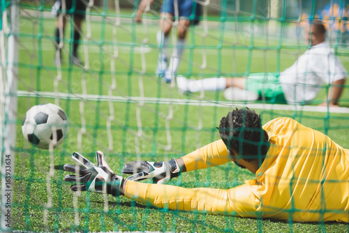 Foto back view of goalkeeper catching ball during soccer match on pitch