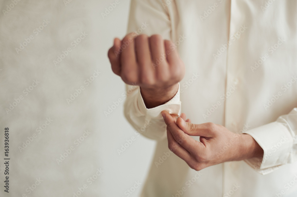 The groom fastens the cufflink on the shirt sleeve close-up The groom fastens the cufflink on the shirt sleeve close-up