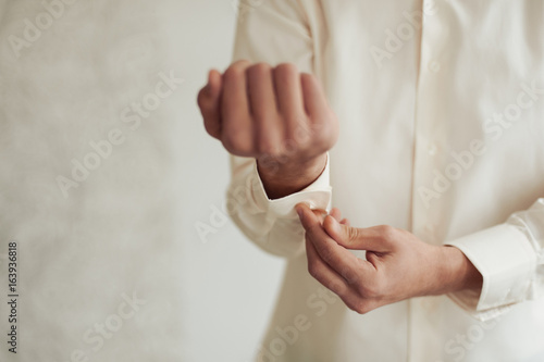 The groom fastens the cufflink on the shirt sleeve close-up