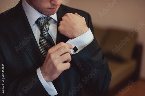 Canvas Print The groom fastens the cufflink on the shirt sleeve close-up