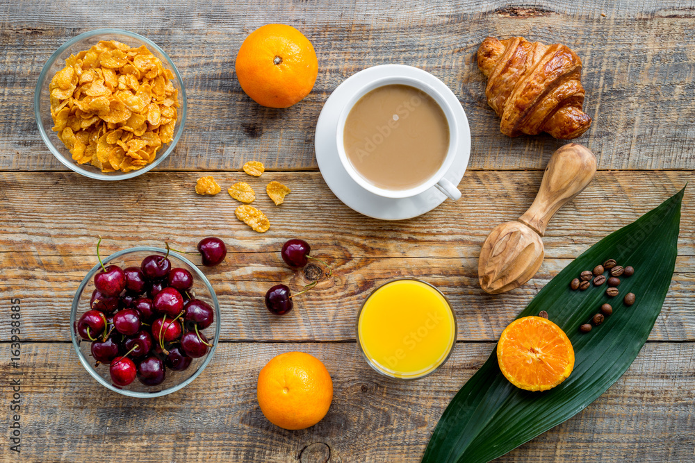 Light summer breakfast. Muesli, oranges, cherry, croissant and coffee on wooden table background top view