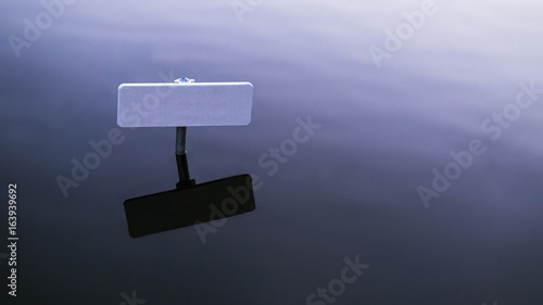 a lone signpost in the water with a pitch black shadow