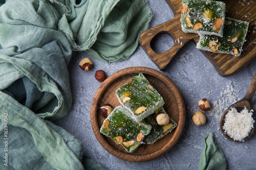Turkish green delight with nuts on wooden brown board and plate standing on grey concrete background. Still life