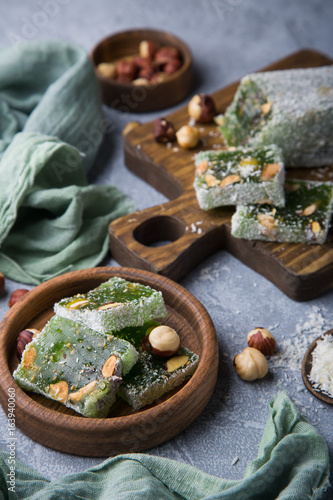 Turkish green delight with nuts on wooden brown board and plate standing on grey concrete background. Still life