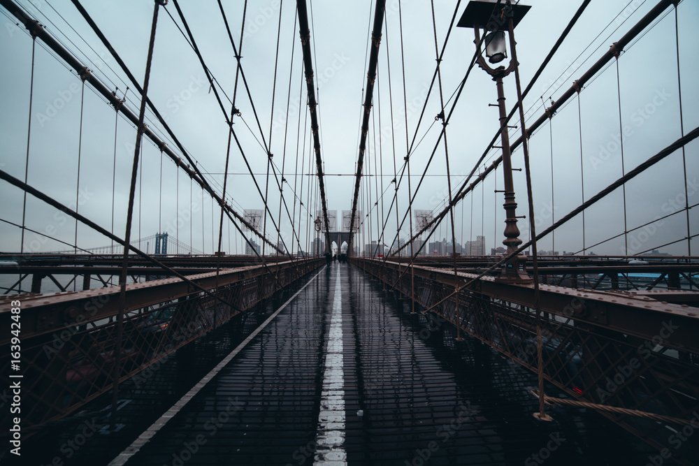 Naklejka premium Brooklyn Bridge: Viewed down the center against NYC skyline on a rainy day