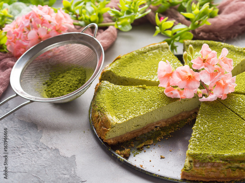 Matcha baked cheese cake and pink flowers on gray concrete background