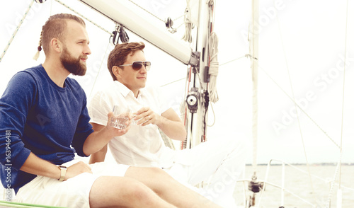 Canvas Print Happy friends sitting together on a deck of a yacht enjoying a good day and having a drink