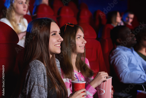 Attractive young cheerful female friends enjoying watching a movie at the cinema together enjoyment recreation entertainment happiness positivity emotions concept.