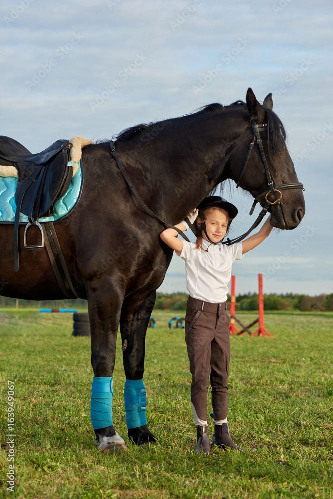 Pretty little girl jockey communicating with her black horse in professional outfit Pretty little girl jockey communicating with her black horse in professional outfit