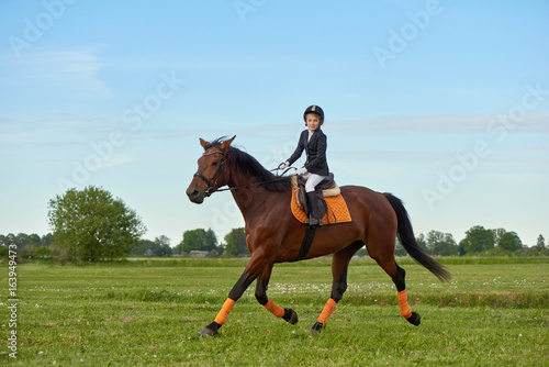 Pretty little girl jockey riding a horse across country in professional outfit