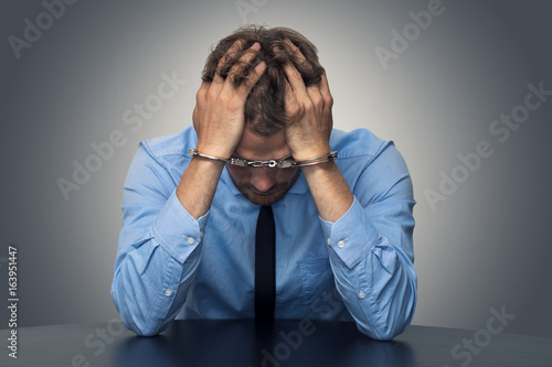 white collar crime concept - desperate businessman with handcuffs photo