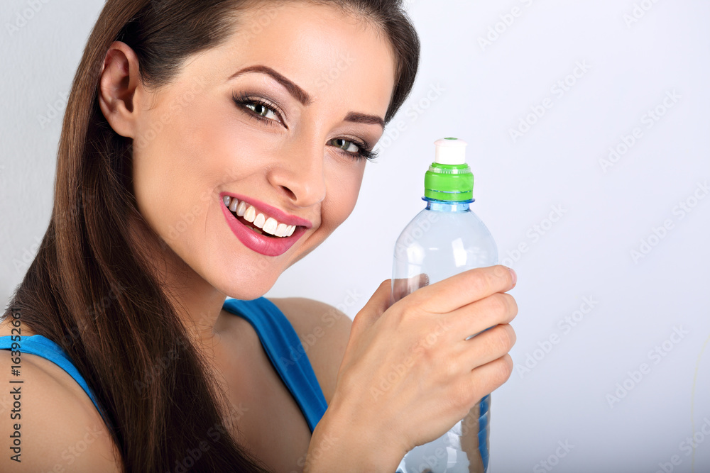 Beautiful happy toothy smiling makeup woman holding and drinking water from the bottle. Closeup portrait on blue background Beautiful happy toothy smiling makeup woman holding and drinking water from the bottle. Closeup portrait on blue background